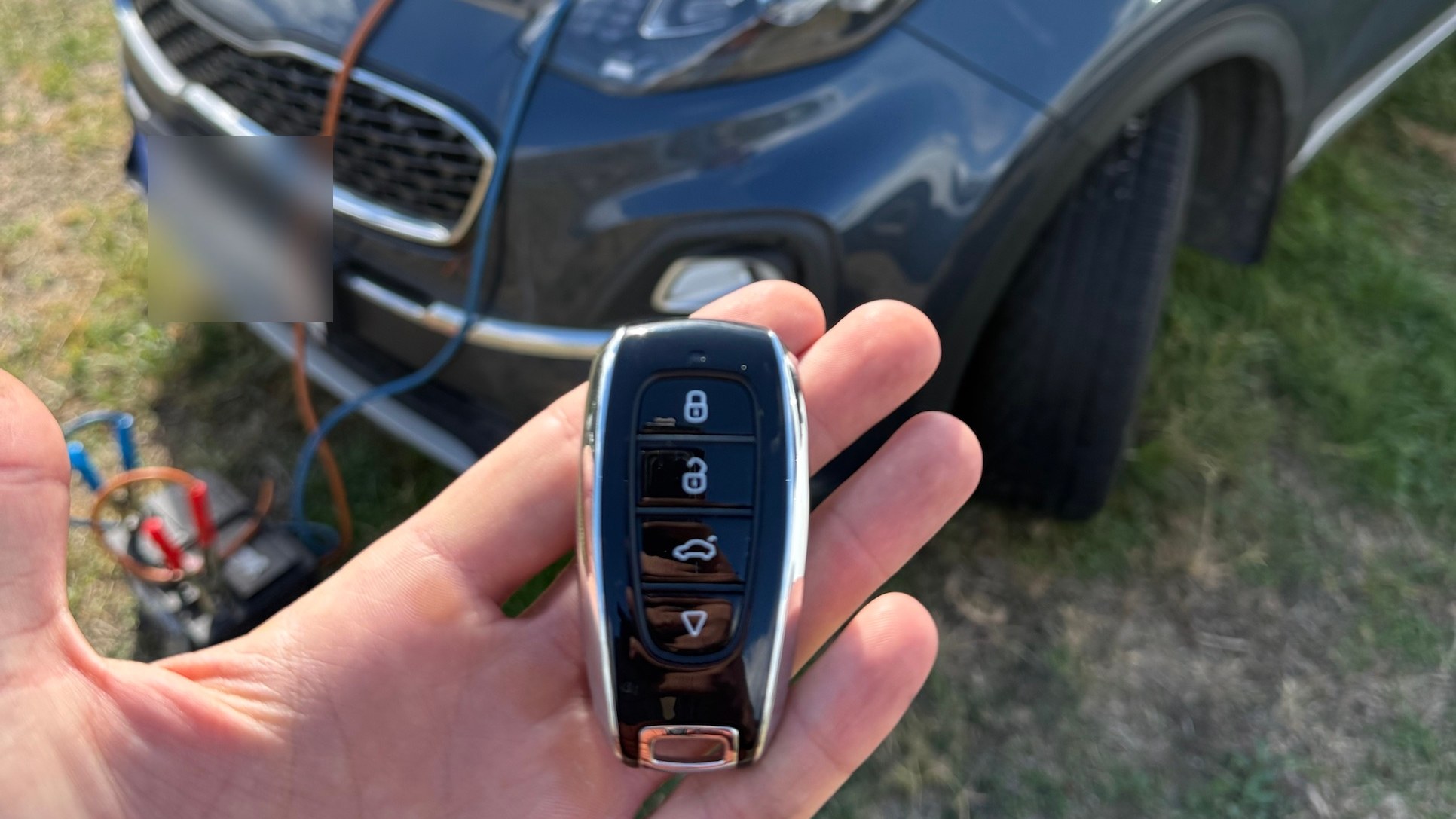 Az új keyless autókulcs a 2021-es Kia Sportage előtt, a motorháztető nyitva, a hordozható áramforrás bekötve