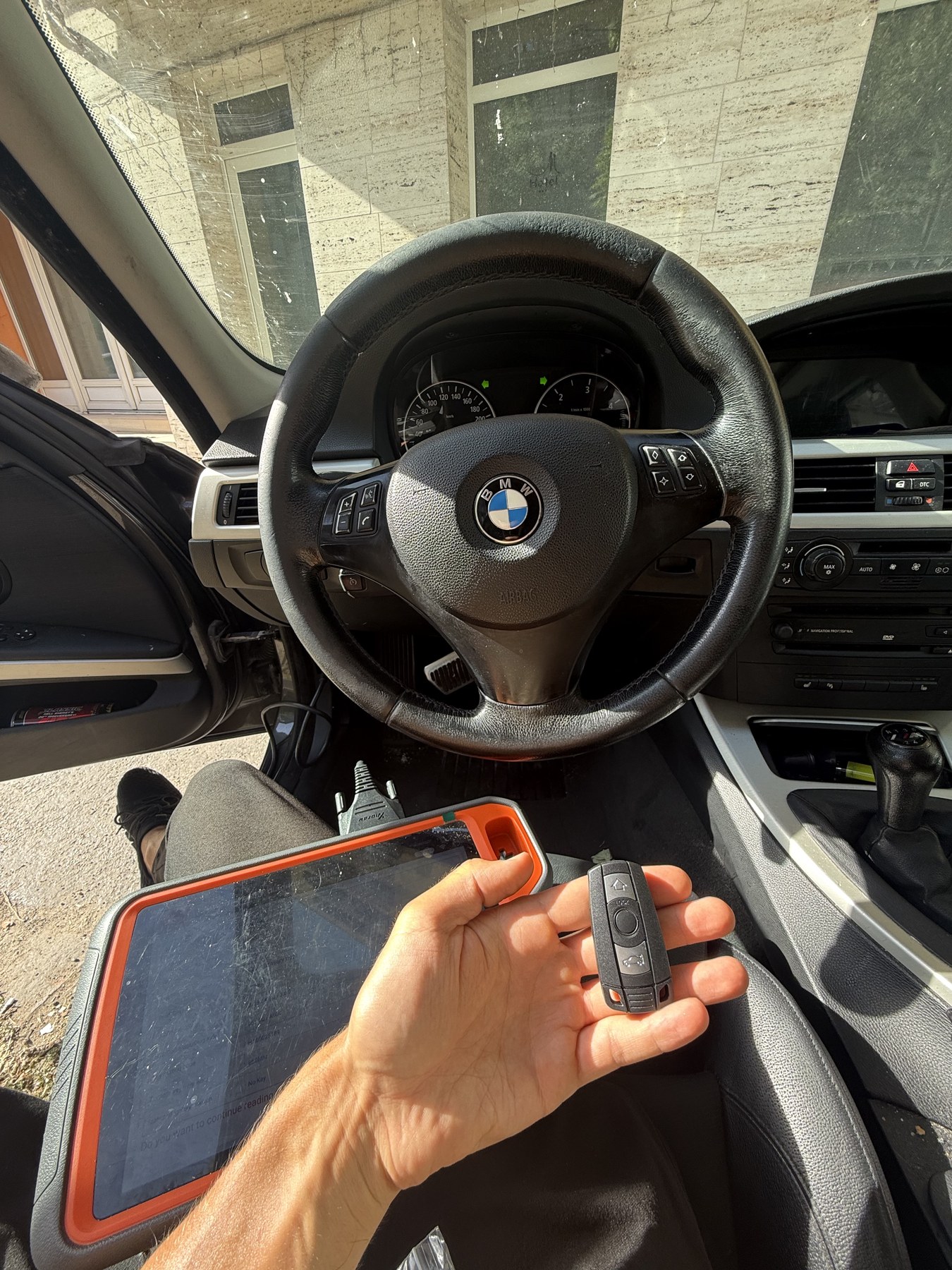 BMW kulcs kézben a jármű utasterében, az ölben a csatlakoztatott diagnosztikai eszközzel