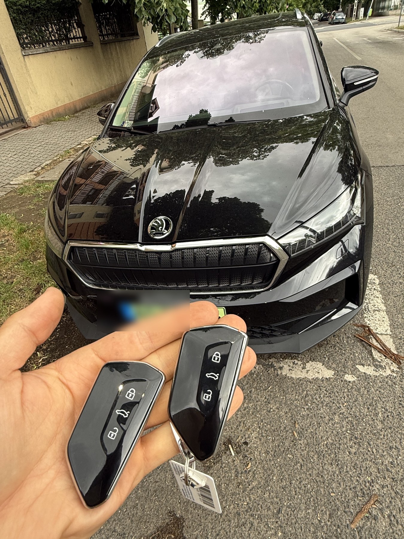 Két új Škoda okoskulcs kézben, mögötte a fekete Škoda az utcán