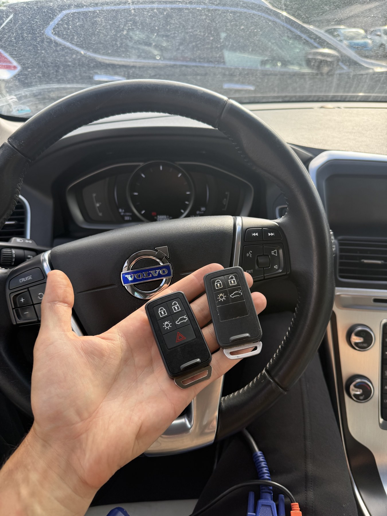 Két elkészült Volvo kulcs kézben a jármű kormánya előtt, alul a csatlakoztatott diagnosztikai kábel